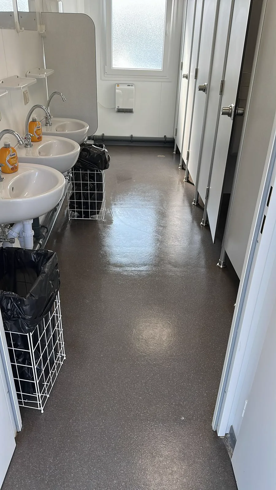 Derselbe Sanitärraum nach der Reinigung mit gleichmäßigem, glänzendem Boden.