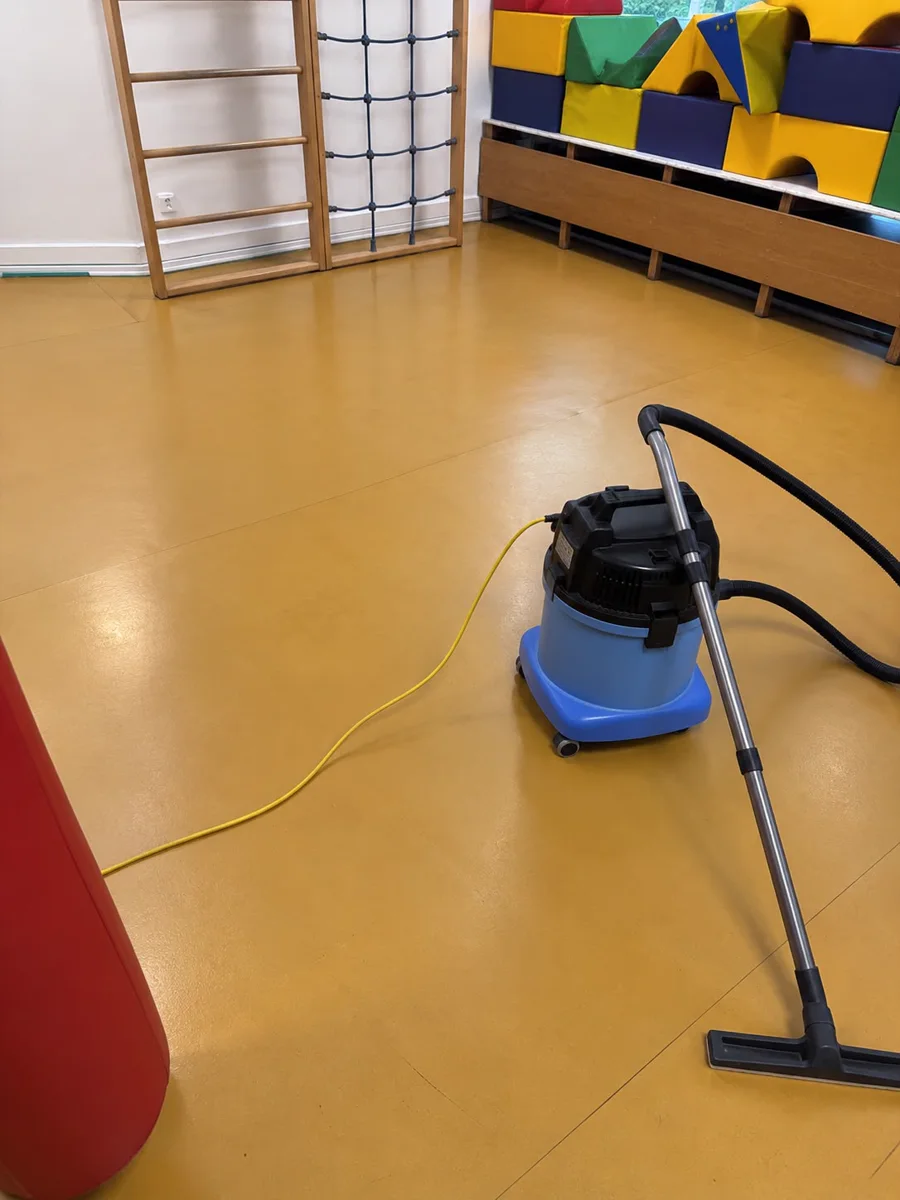 Gereinigter gelber Boden im Bewegungsraum, mit Reinigungsgerät und bunten Turnelementen.